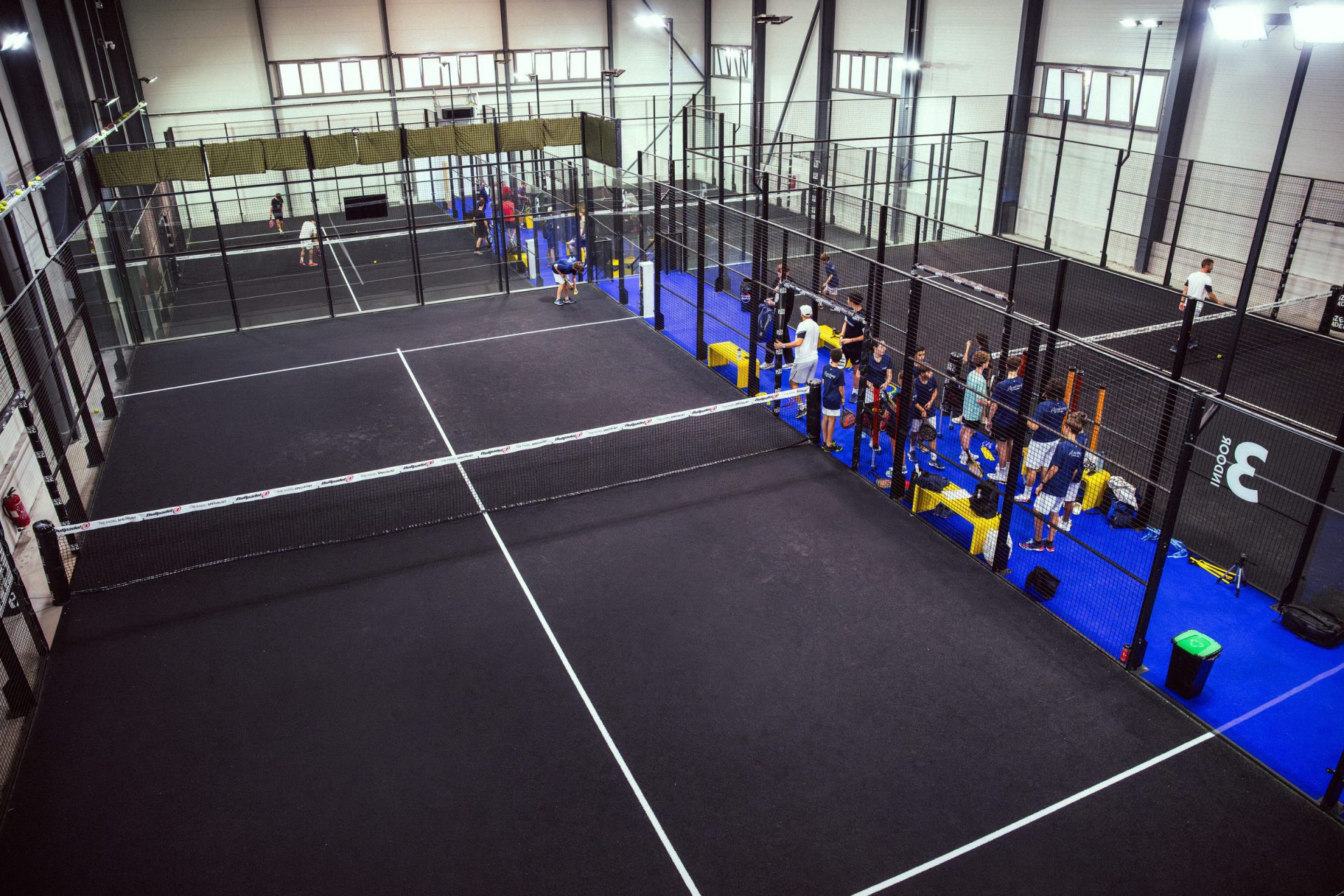Vue large sur une piste de padel indoor du complexe ZE PADEL, joueurs et club autour du terrain